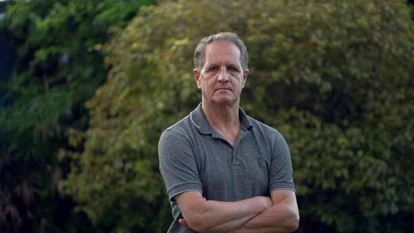 Man standing outdoors with arms crossed in a natural setting.